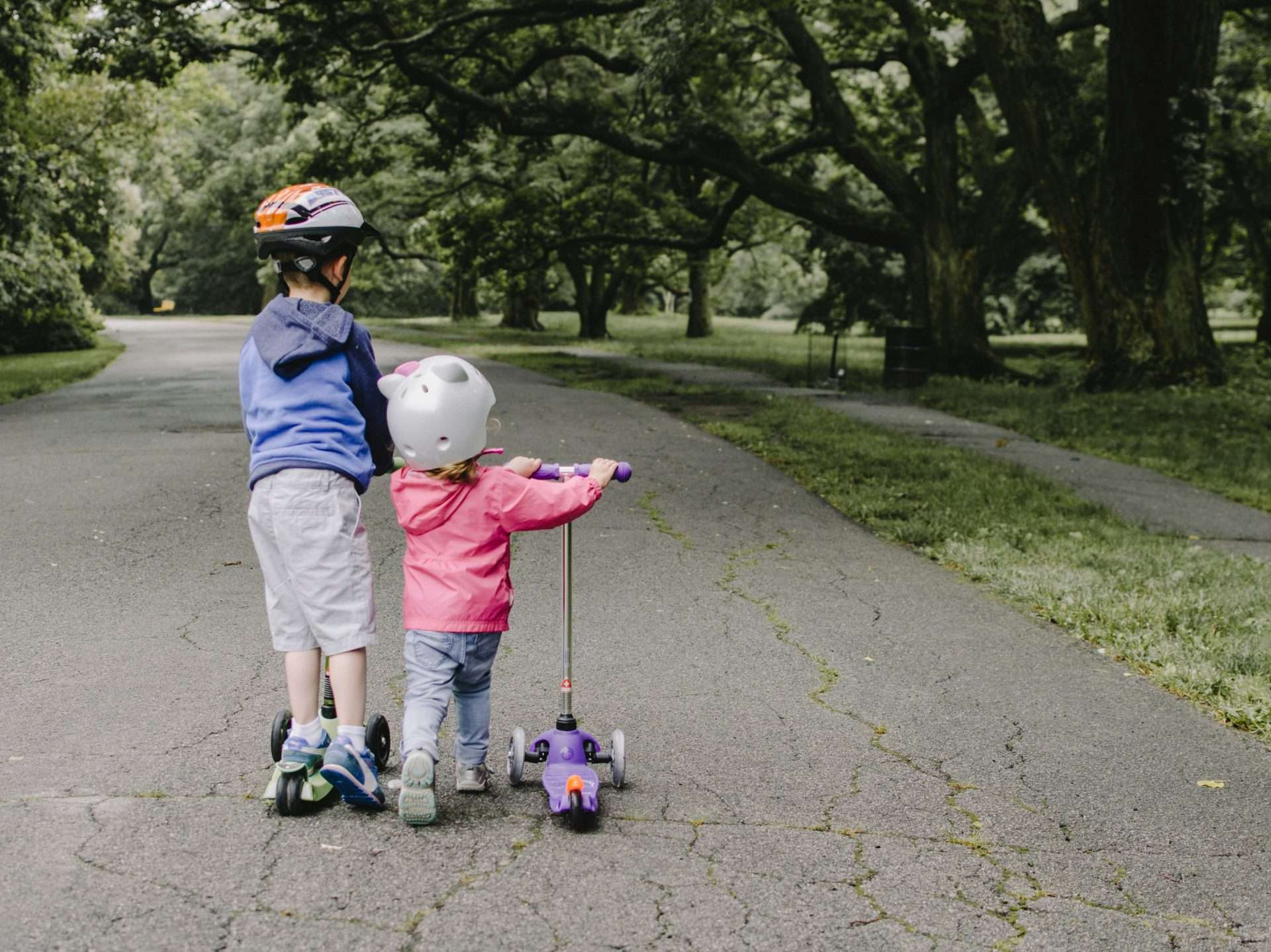 Two children riding scooters on a quiet street