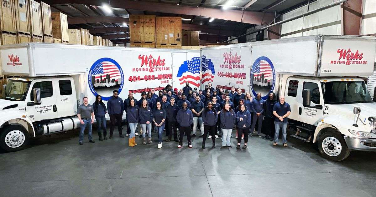 The Atlanta to The Villages movers at Wirks Moving & Storage posing in front of two Wirks branded moving trucks in a storage facility