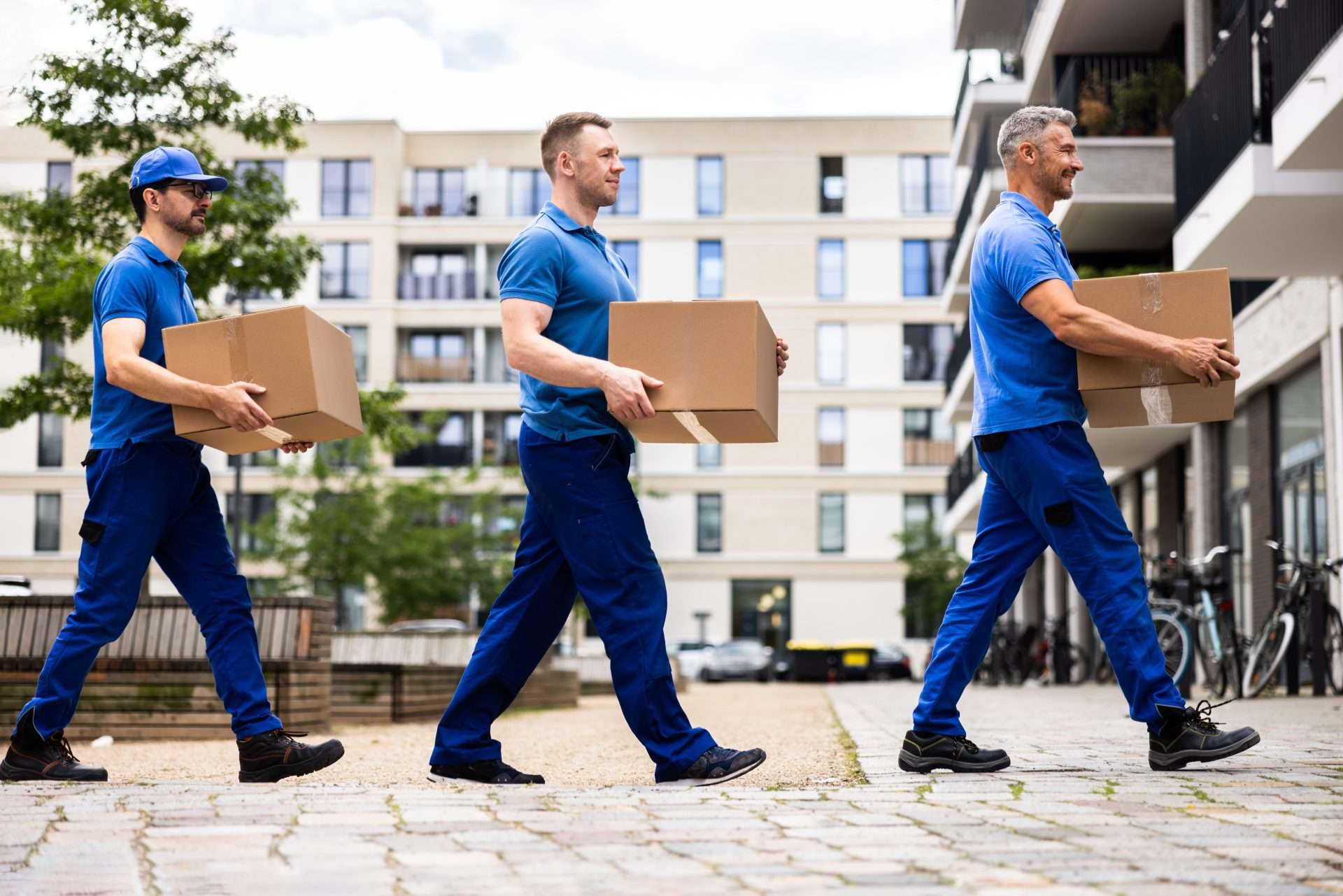 three McDonough movers walking in a line, each carrying a box. 