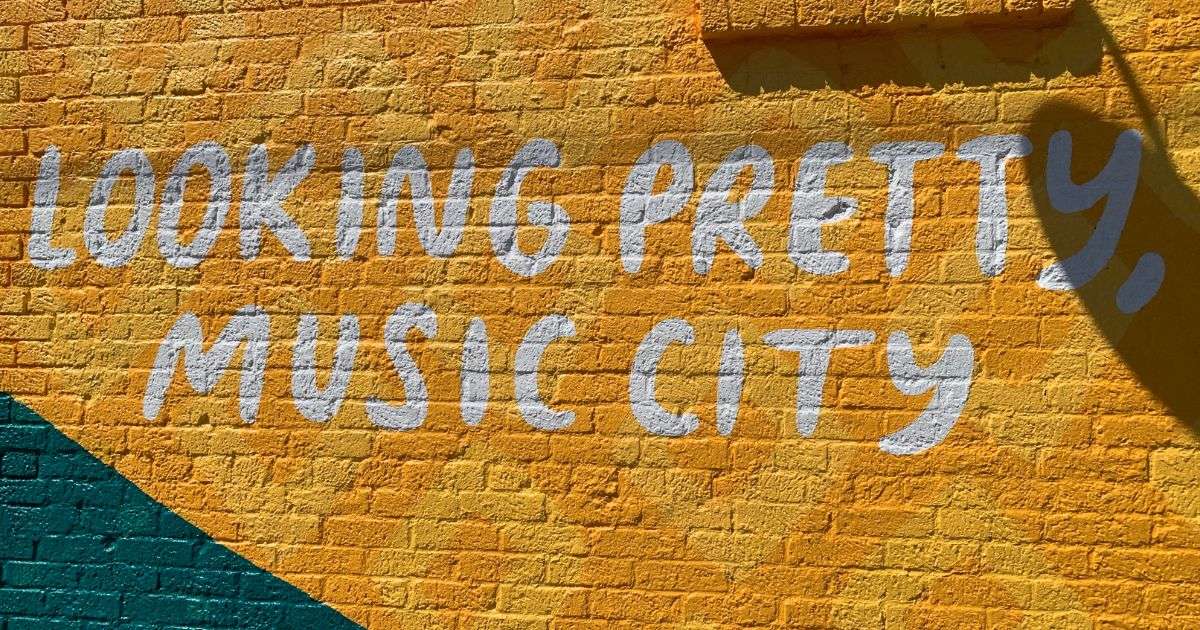 Mural in Nashville with white text saying “Looking pretty, music city” on yellow painted brick