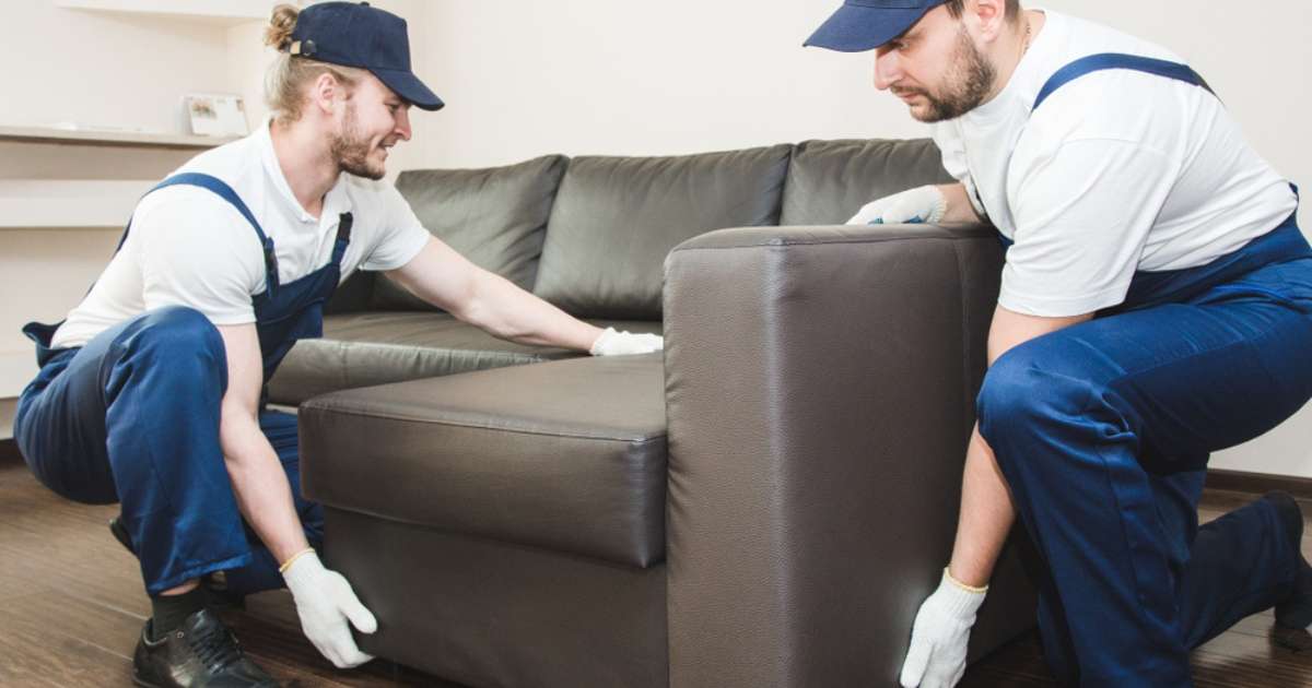 Two movers from a Clermont GA moving company unloading a sofa in a room