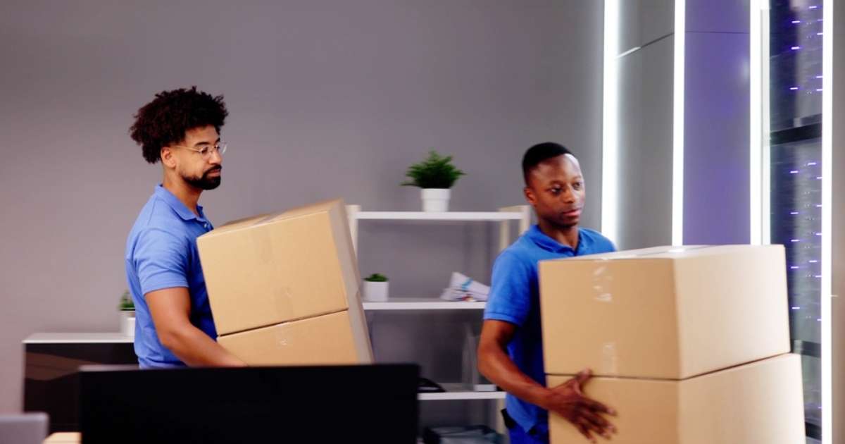 Two movers in Newnan carrying boxes out of a room 