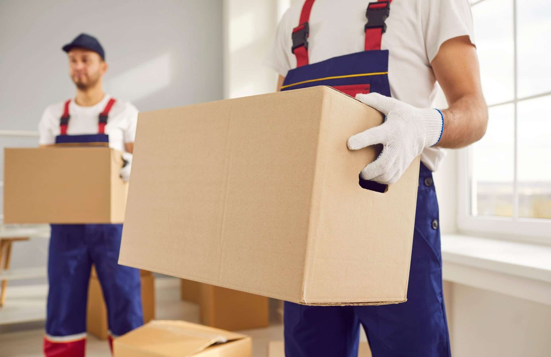  Senoia white glove movers in blue overalls holding boxes inside a customer’s home