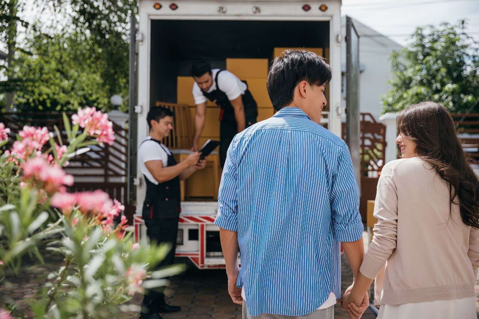 Young couple holding hands and watching Temple GA movers load their belongings into a moving truck