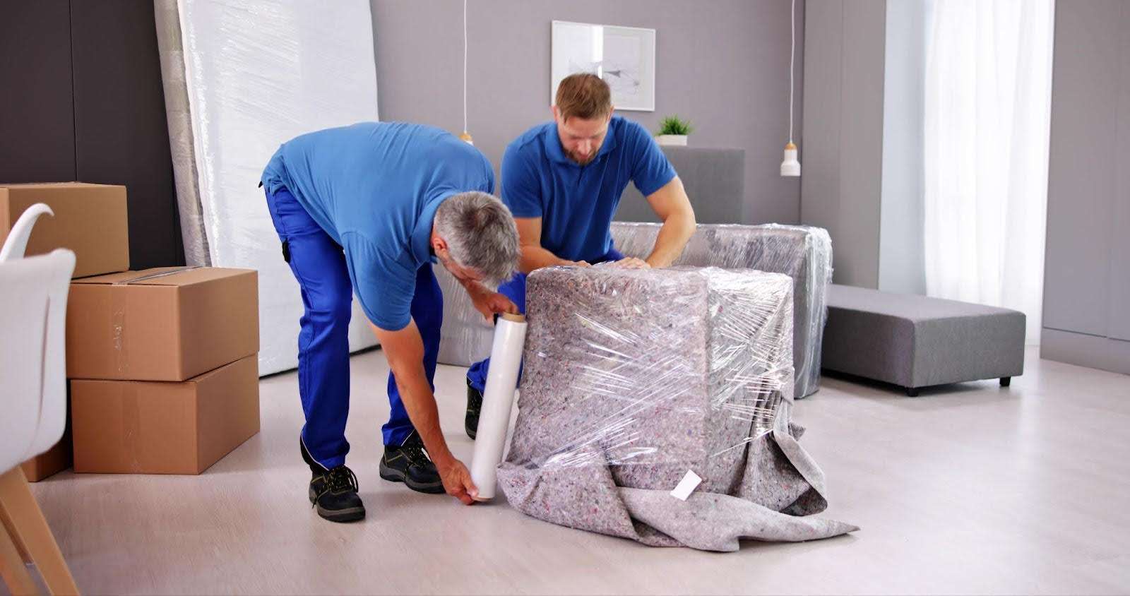 two Morrow GA movers dressed in blue wrapping up furniture in plastic wrap