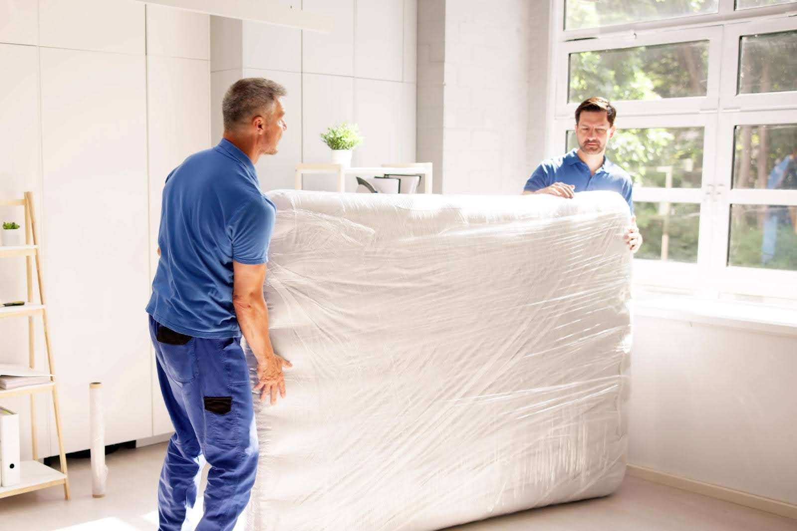 two Morrow GA movers carrying a mattress wrapped in plastic wrap.