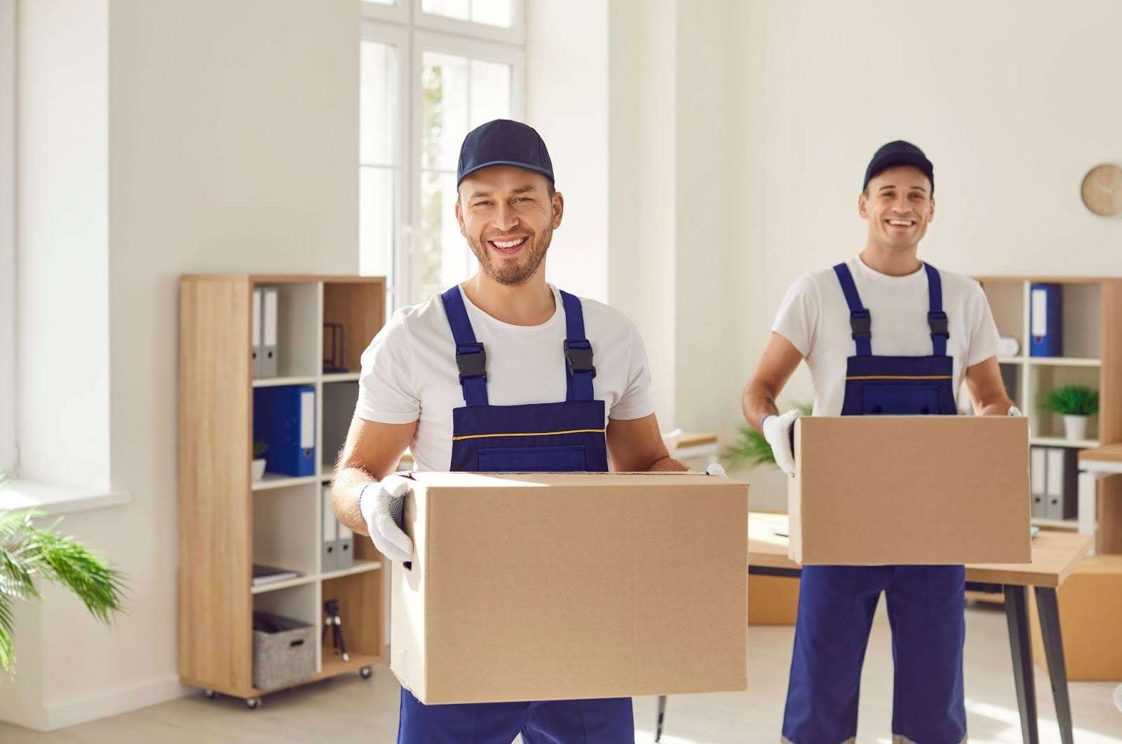 two Alpharetta GA movers in blue overalls holding boxes and smiling