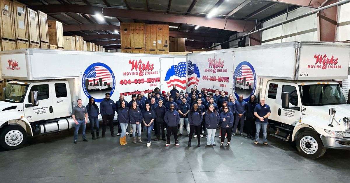 Team of Atlanta to Augusta movers posing in front of two Wirks Moving & Storage moving trucks in the company’s storage facility with wooden storage vaults in the background.