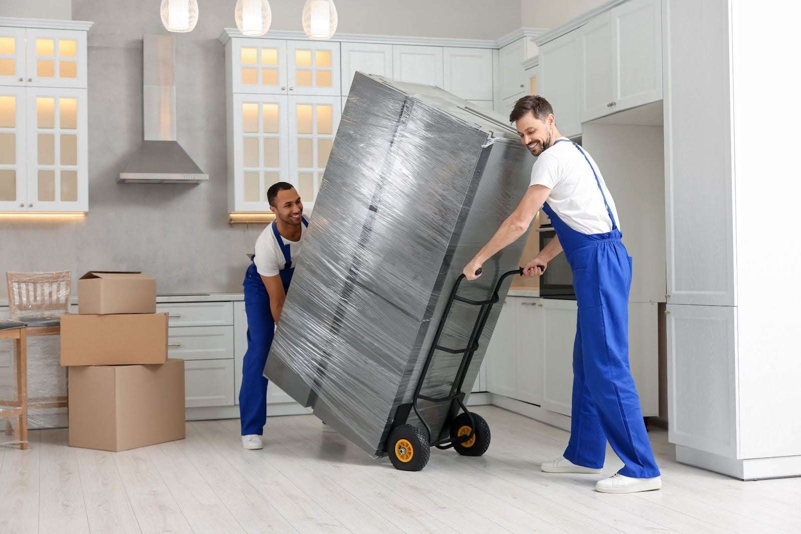 two Canton GA movers wheeling a plastic-wrapped refrigerator into a kitchen