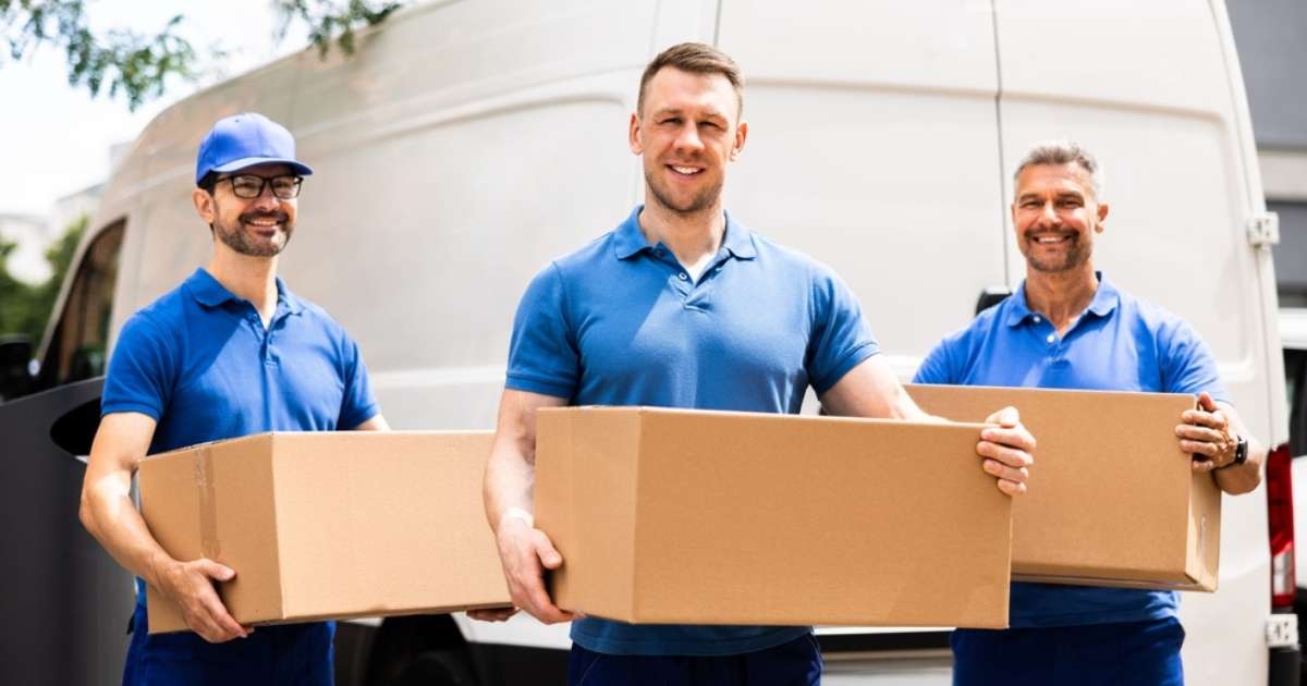 Three Fairburn movers smiling holding moving boxes during a relocation. 